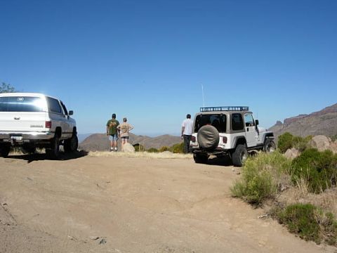 1981 Ford F-150 - Two off-road vehicles are parked on a dirt path with people standing nearby, overlooking a desert landscape.