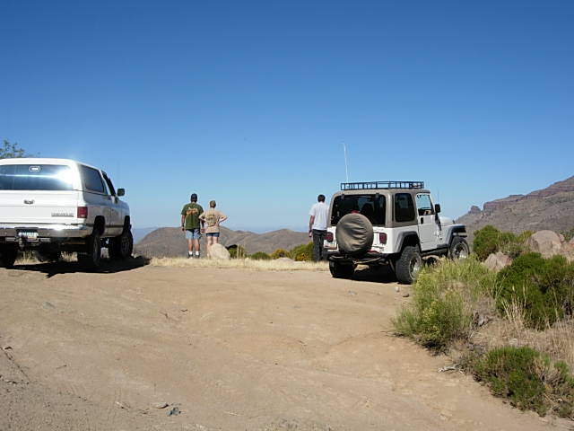 White SUV and silver Jeep parked on dirt road with mountains in background