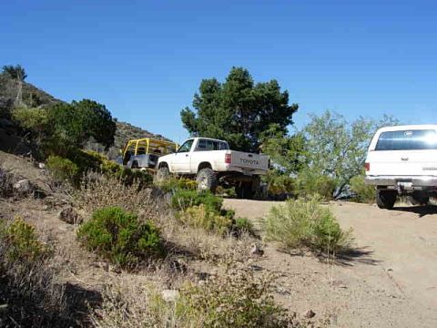 1981 Ford F-150 - A white 1981 Toyota pickup truck is parked on a dirt path alongside a white SUV and a yellow off-road vehicle.