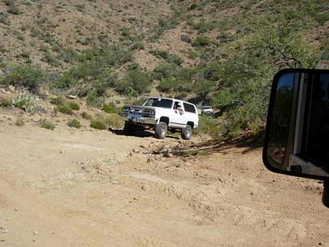 1981 Ford F-150 - A white SUV navigates a dusty, off-road trail with arid hills in the background.