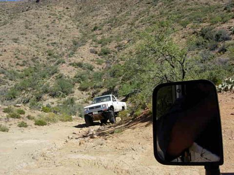 1981 Ford F-150 - A white 1981 Ford F-150 navigates a dusty, off-road path in a desert landscape.