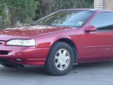 1994 Ford Thunderbird - A red coupe is parked on a concrete surface with trees in the background.