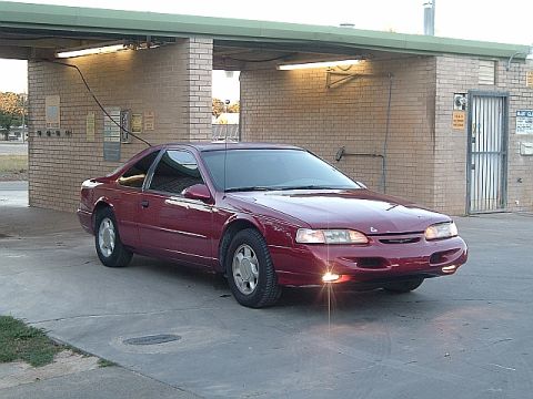 1994 Ford Thunderbird - A red 1994 Ford Thunderbird coupe is parked in front of a brick structure with a covered area.
