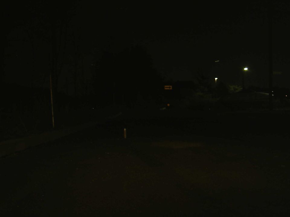 Dark night scene with distant streetlight and glowing right-arrow sign; no vehicle visible