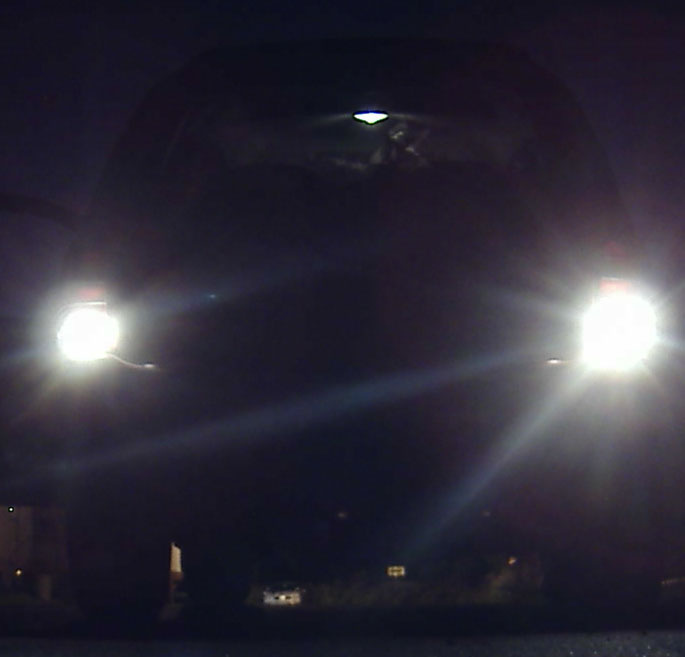 Front of a vehicle at night with two bright headlights on, body obscured by darkness