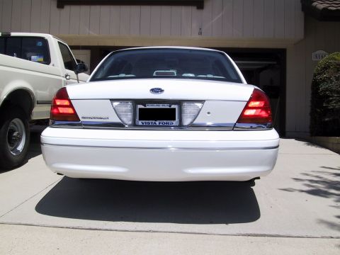 2003 Ford Crown Victoria - The rear of a white Ford Crown Victoria is shown, parked in a driveway with a pickup truck beside it.