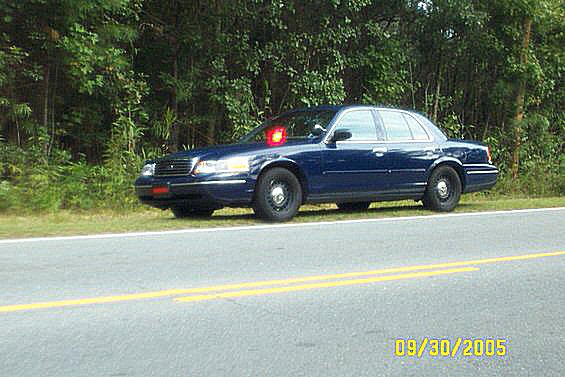 Dark blue Crown Victoria sedan on roadside with red roof beacon and grille lights lit