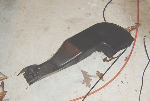 1986 Ford Bronco - A black plastic automotive part lies on a concrete surface, surrounded by electrical wires and fallen leaves.
