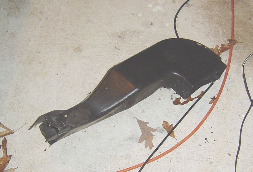 Black plastic automotive part on concrete floor with wires and leaves