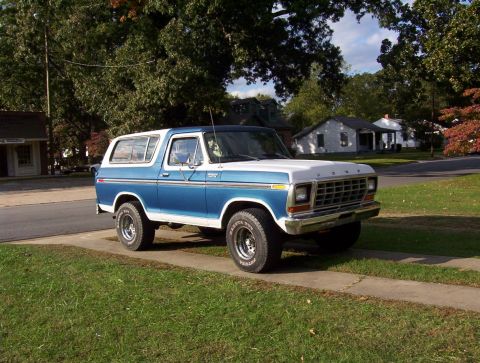 1979 Ford Bronco - This 1979 Ford Bronco, seen from a three-quarter front view, is parked on a sidewalk with a suburban neighborhood in the background.