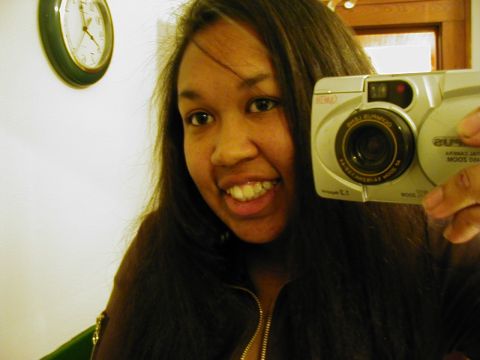 1997 Ford Taurus - A woman smiles while taking a selfie with a digital camera, with a clock visible on the wall behind her.
