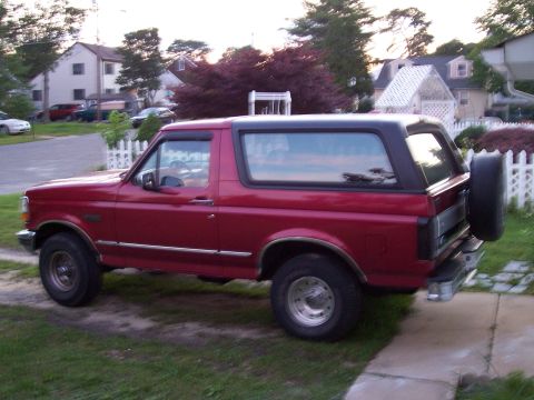 1995 Ford Bronco - Side view of a red 1995 Ford Bronco parked in a driveway with a suburban background.