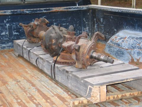 1995 Ford Bronco - Two heavily rusted front axle assemblies are secured to a wooden pallet within the bed of a pickup truck.