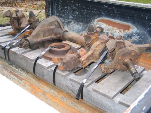 1995 Ford Bronco - Several rusty front axle components and brake rotors are secured to a pallet in the back of a pickup truck.