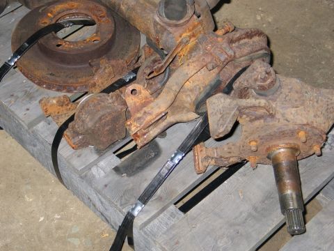 1995 Ford Bronco - Close-up of heavily rusted vehicle axle parts, including a brake rotor and spindle, resting on a wooden pallet.