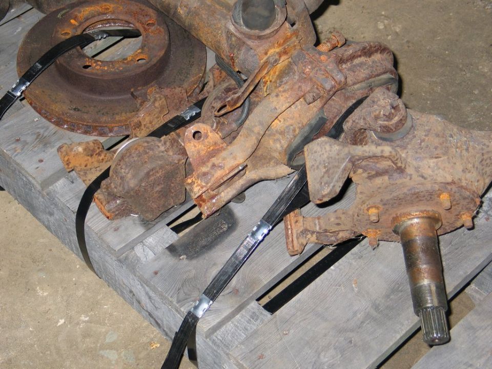Rusted vehicle axle components on a wooden pallet, secured with black straps