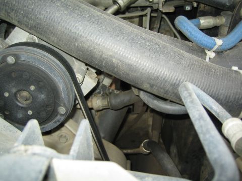 1990 Ford Bronco - Close-up of an engine bay showing a large ribbed radiator hose, a ribbed pulley, and blue secondary hoses among dusty components.