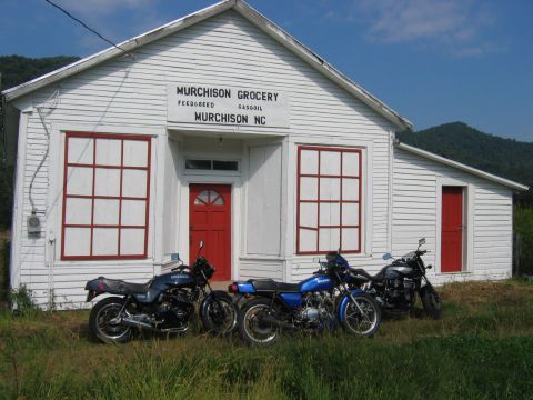 1985 Ford LTD Crown Victoria - Three motorcycles are parked in front of a white building with red trim that says Murchison Grocery.