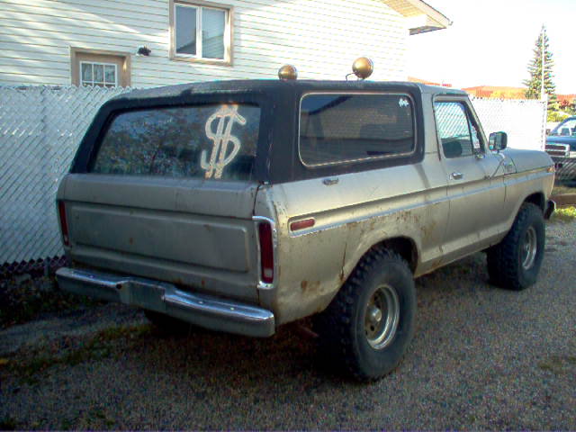 1978 Ford Bronco with dollar sign sticker on rear window, parked on gravel