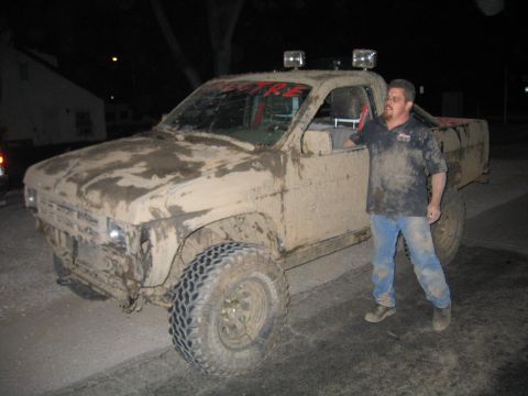 1991 Nissan Pathfinder - A man stands next to a heavily mud-covered 1991 Nissan Pathfinder pickup truck at night.