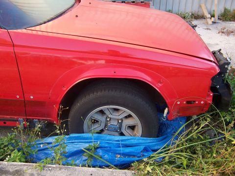 1984 Toyota Celica - A red car's front fender and wheel are visible, with evidence of damage and missing components.