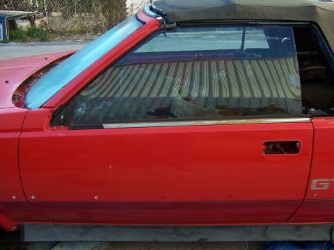 1984 Toyota Celica - A red convertible sports car is shown from the side, with a missing door handle and a torn convertible top.