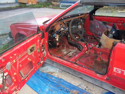 1984 Toyota Celica - The interior of a red convertible is shown with its doors open, revealing a stripped-down cabin and exposed wiring.