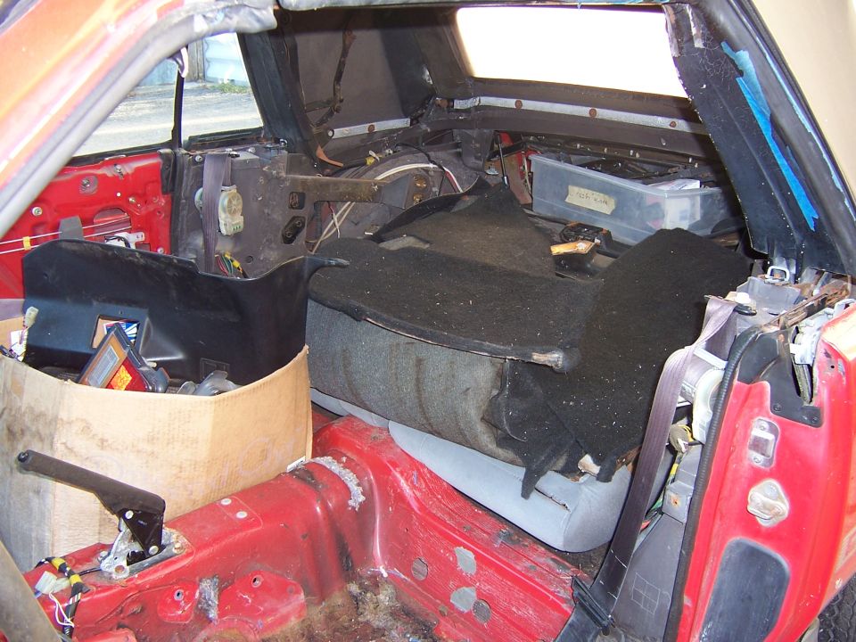 Interior of a red 1984 Toyota Celica with seats removed and parts scattered