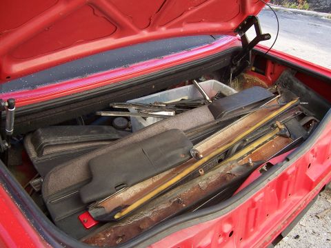 1984 Toyota Celica - The trunk of a red car is filled with assorted automotive parts and trim pieces.