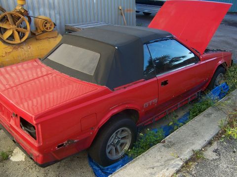 1984 Toyota Celica - Red 1984 Toyota Celica GTS convertible sits with hood open, showing signs of wear.