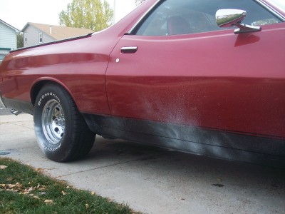 1972 Ford Ranchero - The side of a red pickup truck shows some white spray paint marks along the lower body panel.