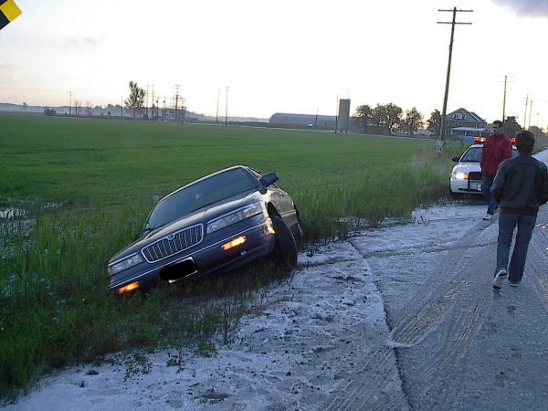 Dark blue Grand Marquis in a ditch with front-corner damage and a police cruiser nearby