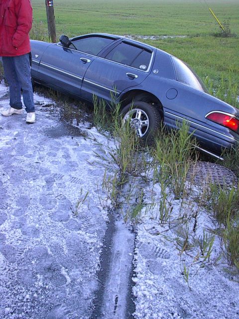 1985 Mercury Grand Marquis - A blue sedan is partially off the road and in a ditch, with a person standing on the shoulder.