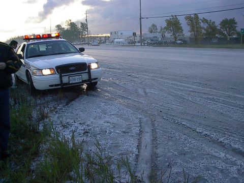 1985 Mercury Grand Marquis - A police car is stopped on the side of a road covered in white debris.