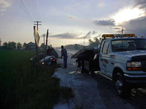 1985 Mercury Grand Marquis - A tow truck is on the scene assisting a car that has gone off the road into a ditch.