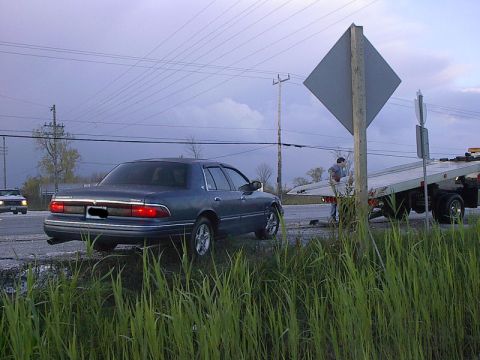 1985 Mercury Grand Marquis - A blue Mercury Grand Marquis is parked on the side of the road with a tow truck in the background.