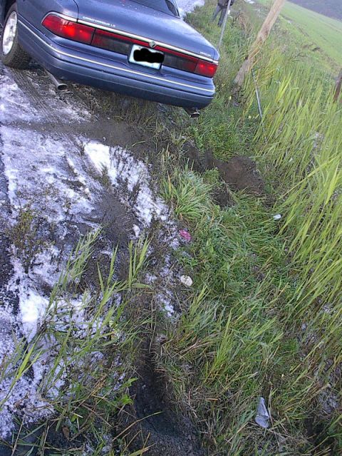 1985 Mercury Grand Marquis - A blue sedan is stuck on a muddy embankment, with its rear end angled towards the grass.