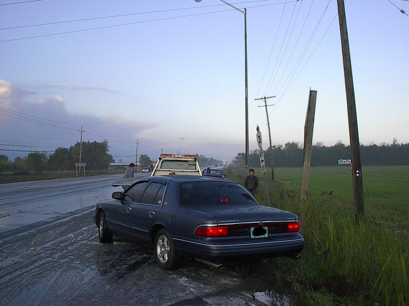 Blue-gray Mercury Grand Marquis LS on muddy shoulder with tow truck ahead