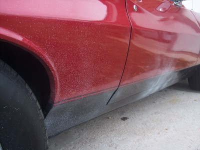 1972 Ford Ranchero - The side of a red car shows a glittery paint job and black trim along the rocker panel.