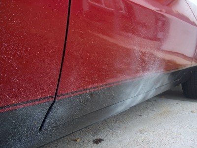 1972 Ford Ranchero - Close-up of a red vehicle's side panel, showing dust accumulation on the black trim.