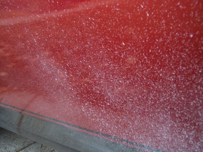 1972 Ford Ranchero - A close-up of a red car door shows a surface covered in numerous white specks.