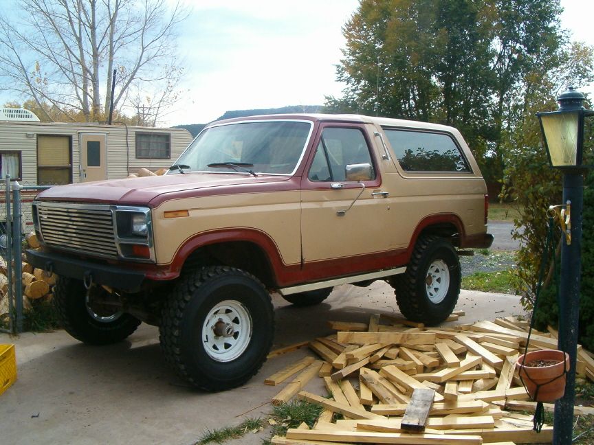 Red and tan two-tone Ford Bronco lifted on white wheels over scattered lumber
