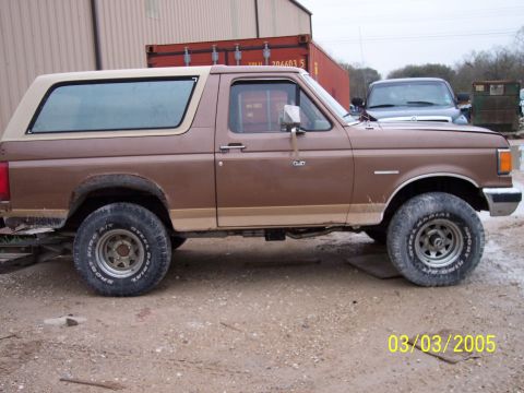 1987 Ford Bronco - Side view of a 1987 Ford Bronco parked outdoors with another vehicle in the background.