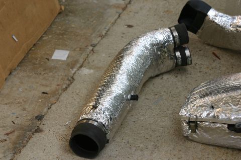 1994 Ford Bronco - Foil-wrapped insulated flexible ducting with black rubber end couplers secured by metal band clamps, laid out on a concrete surface next to…