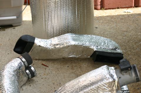 1994 Ford Bronco - Several foil-insulated flexible ducts with black rubber couplers and metal hose clamps, laid out on a concrete surface for what appears to…