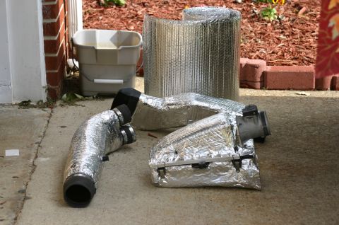 1994 Ford Bronco - Several foil-wrapped insulated ductwork pieces with plastic connectors and a roll of reflective insulation sit on a concrete surface near a…