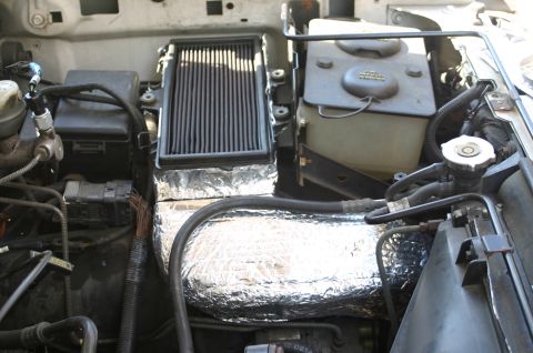 1994 Ford Bronco - Engine bay view showing a black aftermarket-style panel air filter, a translucent brake/clutch fluid reservoir, and heat-reflective foil in…