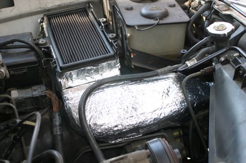 1994 Ford Bronco - Engine bay view showing a black finned intercooler or cooler mounted at the top, with an air intake tube and ducting wrapped extensively in…