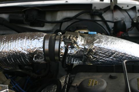 1994 Ford Bronco - Close-up of an engine bay showing a large air intake tube wrapped in reflective heat-shielding foil, connected via a black rubber coupler w…