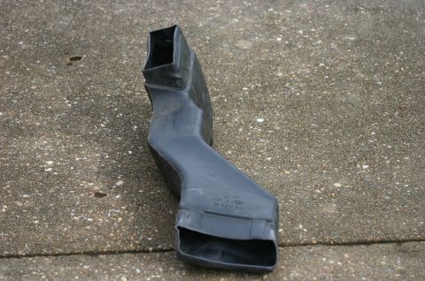 1994 Ford Bronco - A black molded plastic air duct or ventilation channel lying on a concrete surface, with a squared inlet at one end and a rectangular flare…